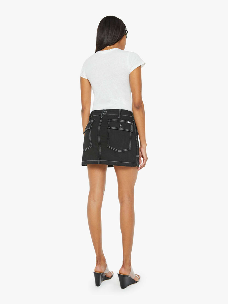 Back view of a woman in a black high-waisted mini skirt with a button fly, oversized patch pockets and a hem that hits mid-thigh.