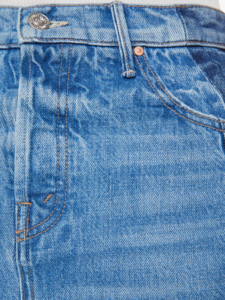 Swatch view of a woman in a denim maxi skirt with a high rise, thigh-high back slit and a frayed ankle-length hem in a mid blue and dark panels down the outer leg.