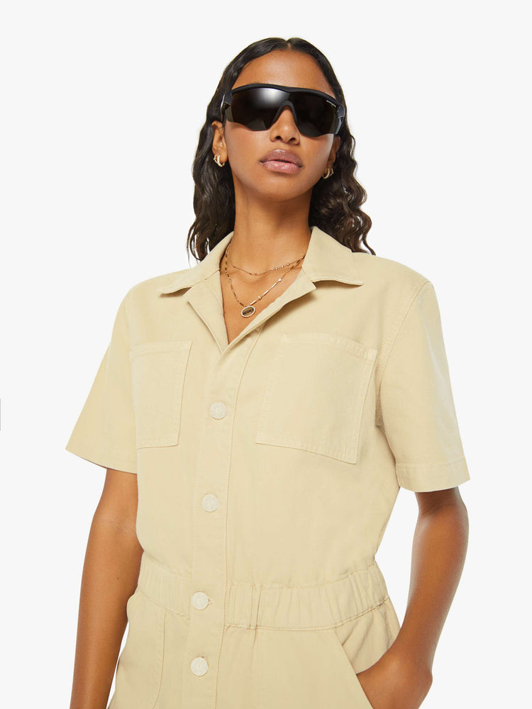 Swatch view of a woman in a light khaki V-neck romper with a notched collar, short sleeves, patch pockets, buttons down the front and an elastic waistband.