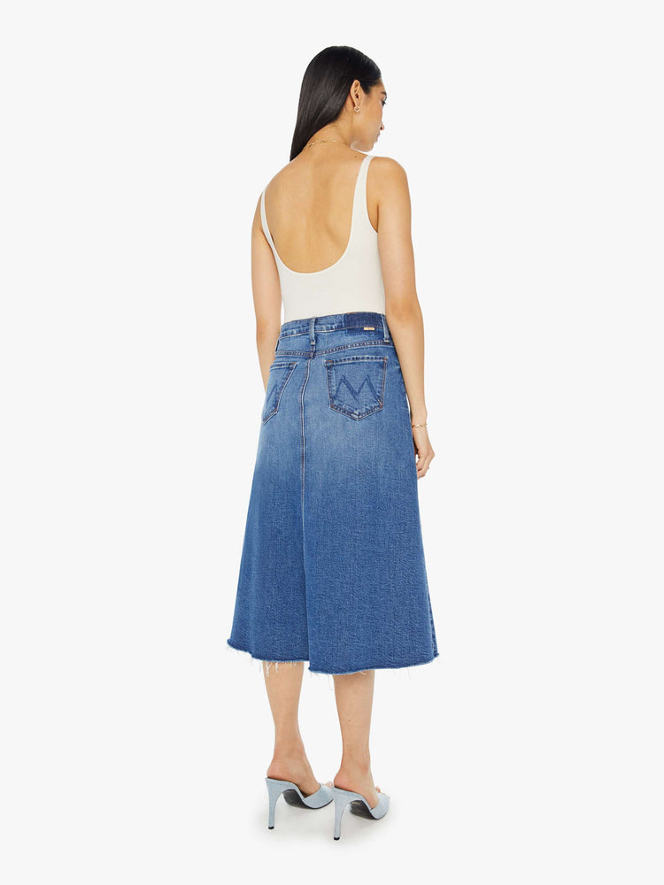 Back view of a woman high waisted midi skirt with an A-line fit and a frayed hem in medium blue wash.