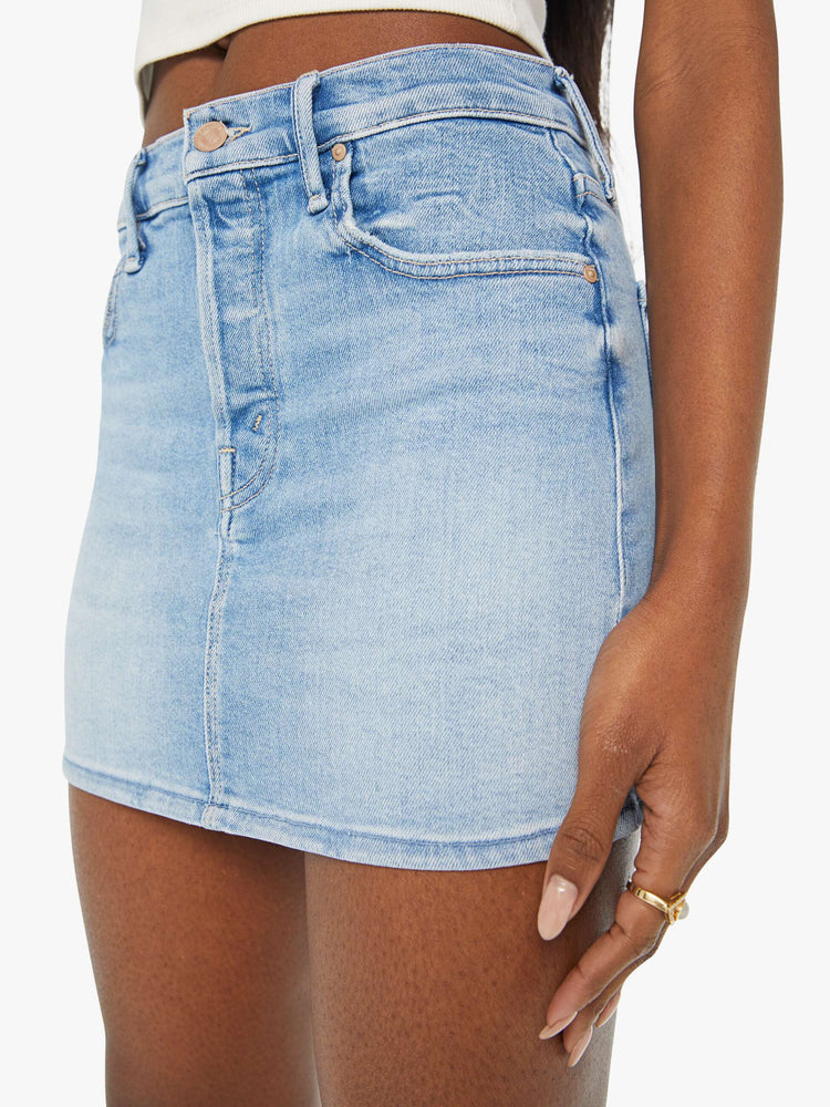 Close up view of a woman denim mini skirt designed to be worn lower on the hips with a button fly, slim fit and thigh-grazing hem in a light blue wash.