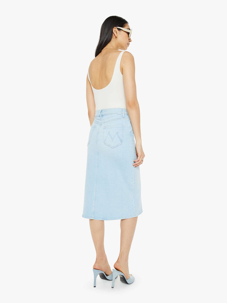 Back view of woman in a high-waisted denim midi skirt with an A-line fit and a calf-length hem in a light blue wash.