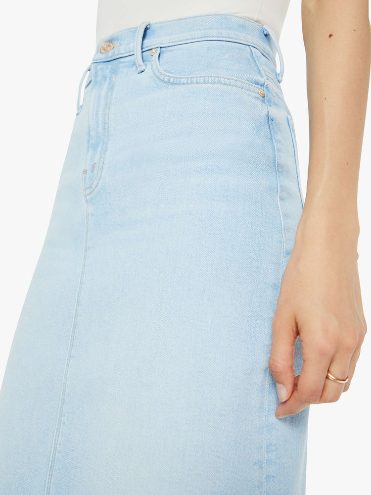 Close up view of woman in a high-waisted denim midi skirt with an A-line fit and a calf-length hem in a light blue wash.