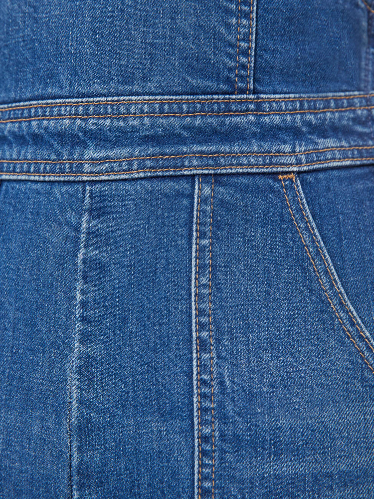 Swatch view of a woman in mid-blue denim overalls with a high rise, wide straight leg, patch pockets and a long 32-inseam with a clean hem.