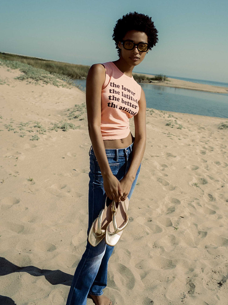 Editorial image of a woman at the beach, wearing a peach tank top and dark blue jeans.