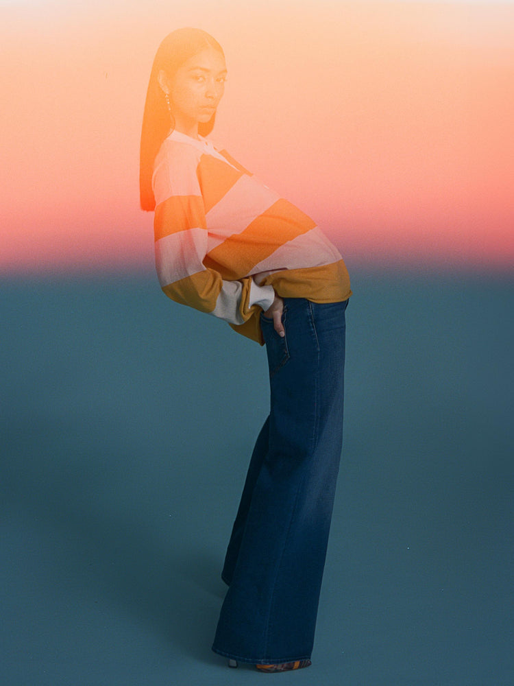 An editorial image of a woman leaning back, wearing a dark blue wash wide leg jean and a striped rugby polo.