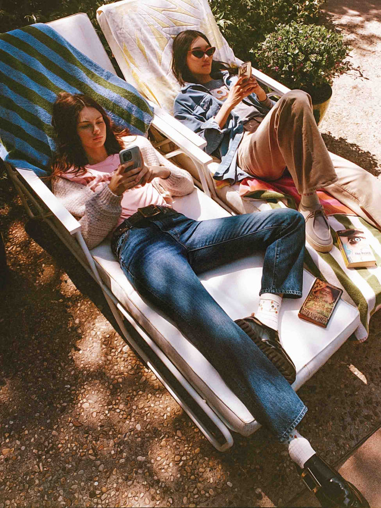 An editorial image a two women sitting on lawn chairs looking at their phones.