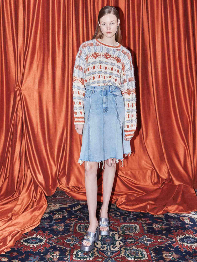 An editorial image of a woman wearing a frayed denim skirt and a knit cardigan.