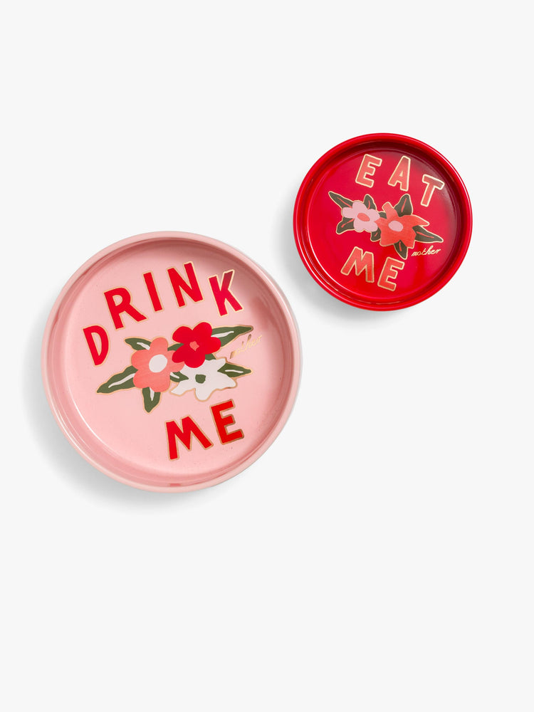 A set of two ceramic dog bowls with a little encouragement from MOTHER. Designed in pink and red, each bowl features a flower motif and text on the bottom.