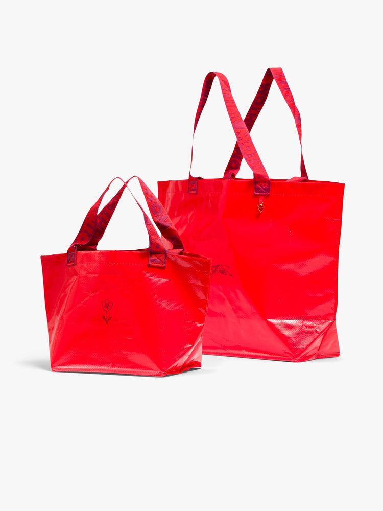 Front view of a set of two, the red bags feature a boxy, oversized shape, roomy interior, internal pocket, charm, thick branded straps and a pink dust bag.