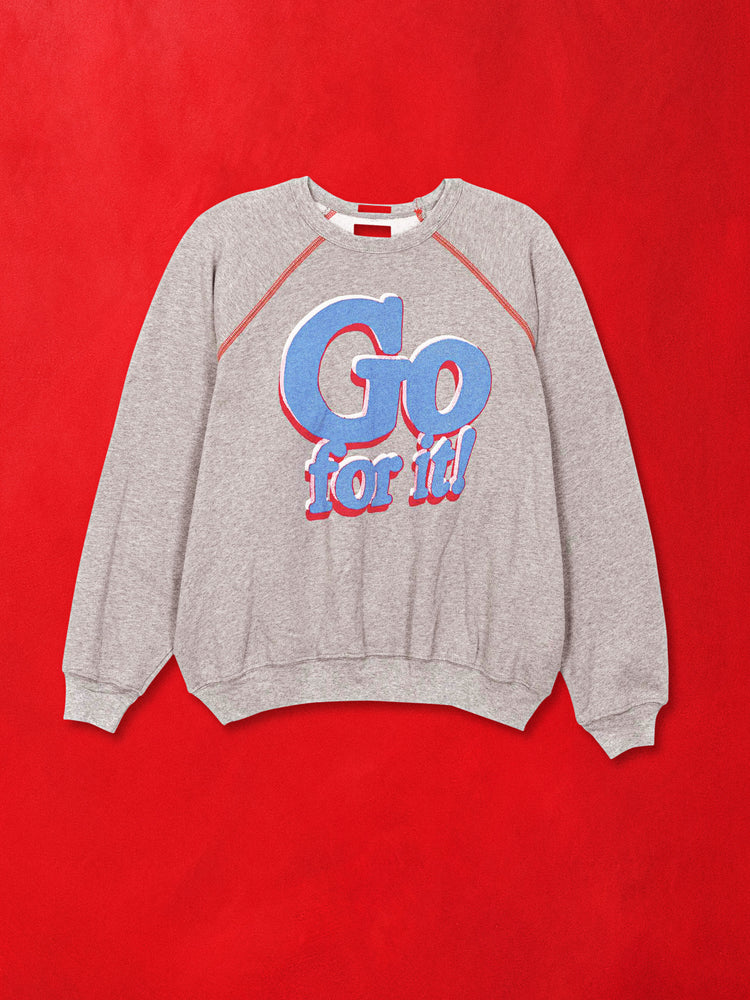 A flat product image of a grey sweatshirt with a blue graphic against a red background.