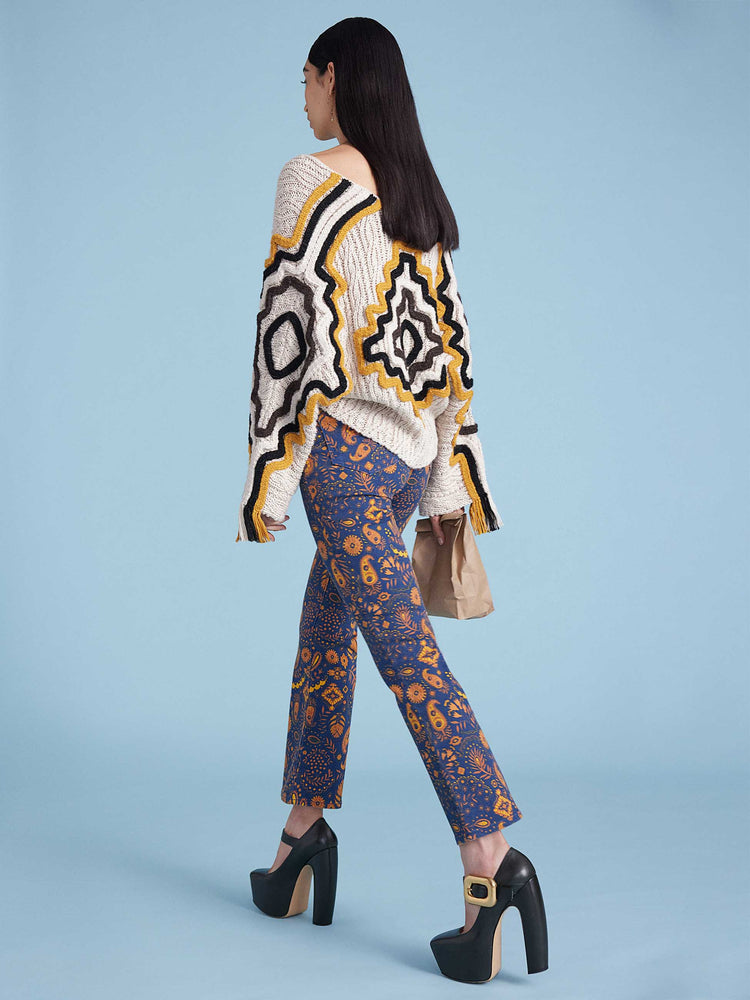 An editorial image of a woman wearing a floral printed pant, a knit cardigan with large embroidery details and fringe.