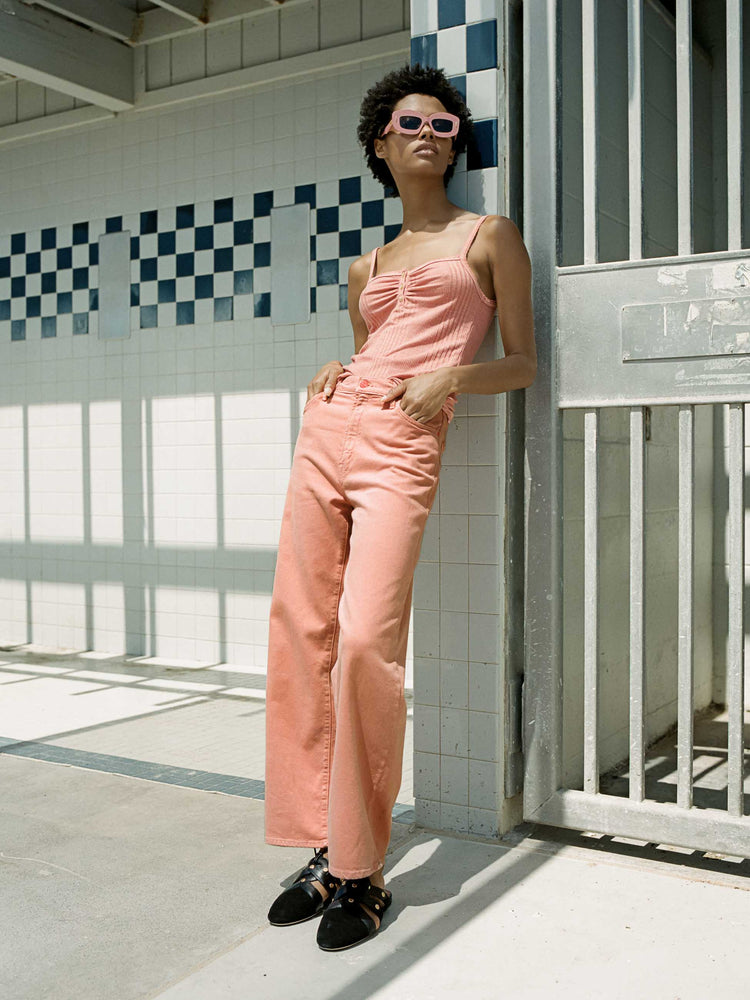 Editorial image of a woman leaning against a tile wall, wearing mango color pants.