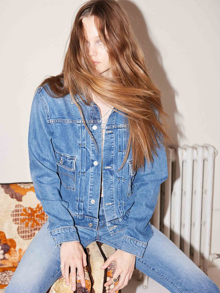 An editorial image of a woman sitting on a couch, wearing a blue denim jacket and matching jeans.