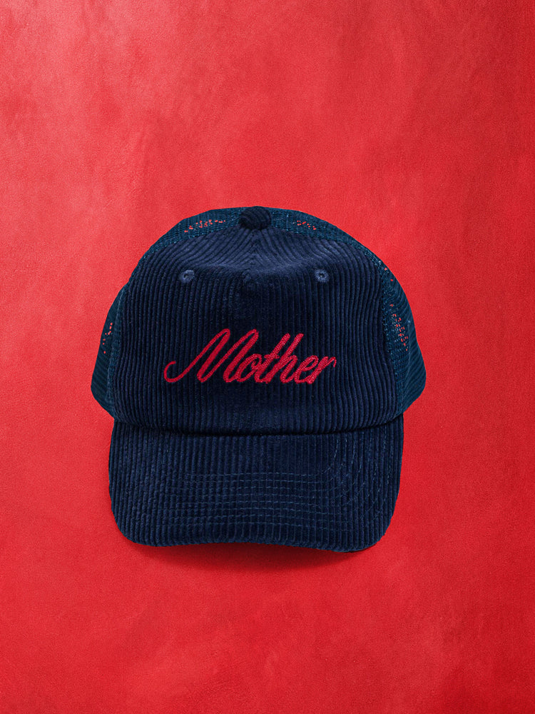 Flat product image of a dark navy blue corduroy hat with Mother embroidered in red against a red background.