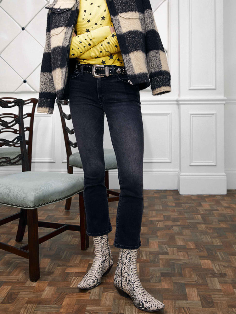 An editorial image of a woman wearing a yellow thermal with a star print, under a plaid jacket and faded black jeans.