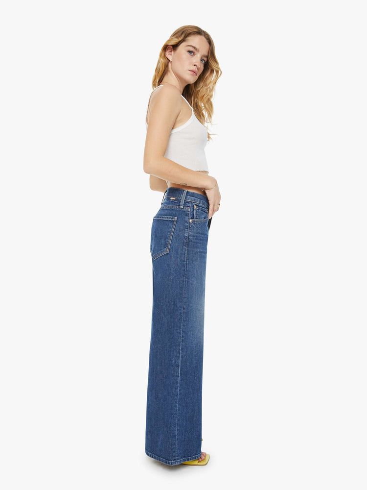 Side view of a petite woman wide-leg jeans feature a button fly, low-set back pockets, high rise with a slouchy fit and a long inseam in a dark blue wash.