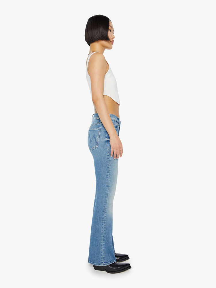 Side view of a petite woman in a light blue mid rise flare jean.