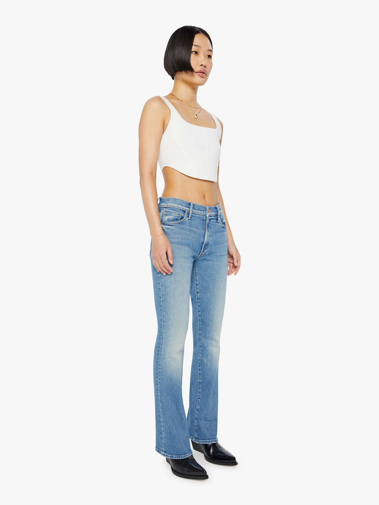 Side angle view of a petite woman in a light blue mid rise flare jean.