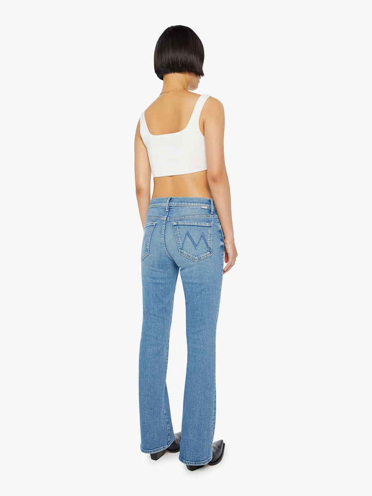 Back view of a petite woman in a light blue mid rise flare jean.