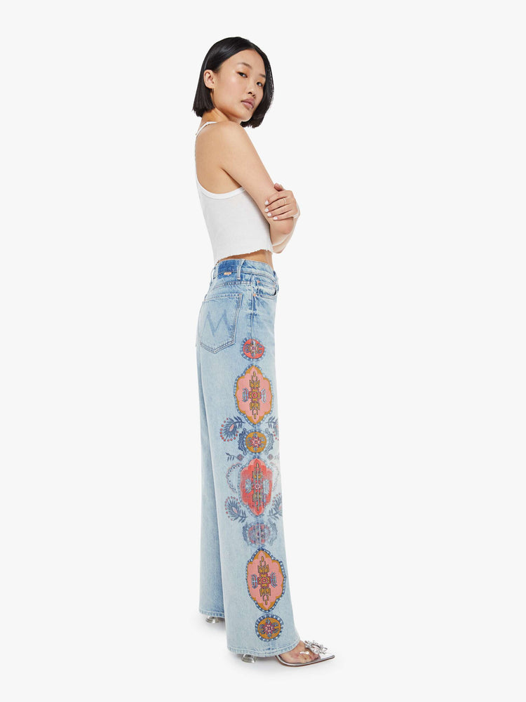 Side view of a high rise wide leg jean in a light blue wash with printed pattern down the side of each leg.