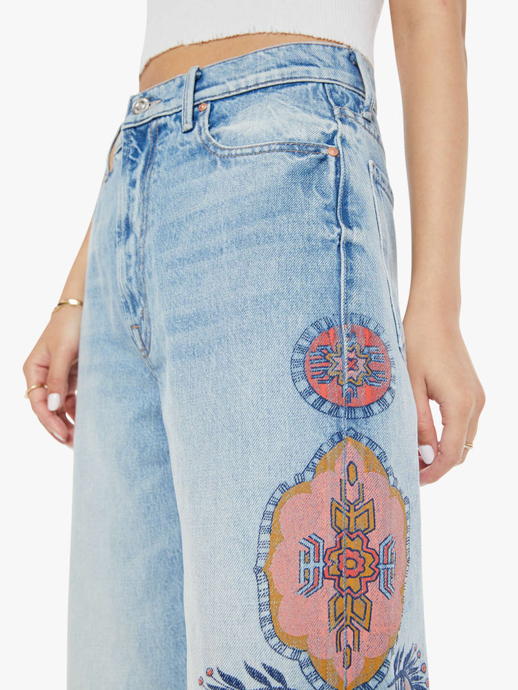 Close up waist view of a high rise wide leg jean in a light blue wash with printed pattern down the side of each leg.