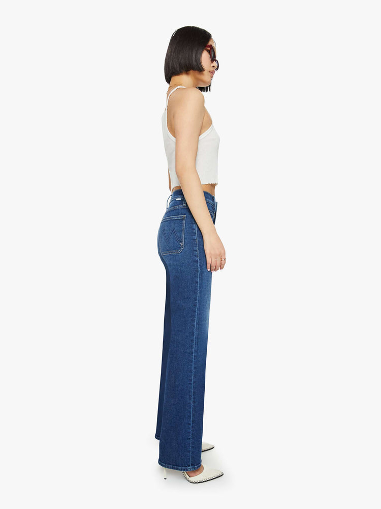 Side view of a petite woman in a dark blue high-waisted jeans with a wide straight leg, zip fly, patch pockets and a long 30-inch inseam with a clean hem. 