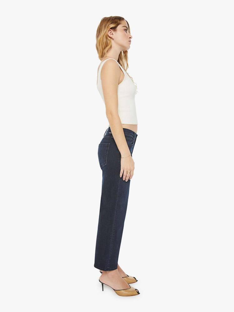 Side view of a petite woman in a dark denim mid-rise jean with a wide straight leg, zip fly and clean ankle-length inseam.