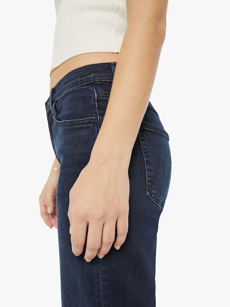 Close up view of a petite woman in a dark denim mid-rise jean with a wide straight leg, zip fly and clean ankle-length inseam.