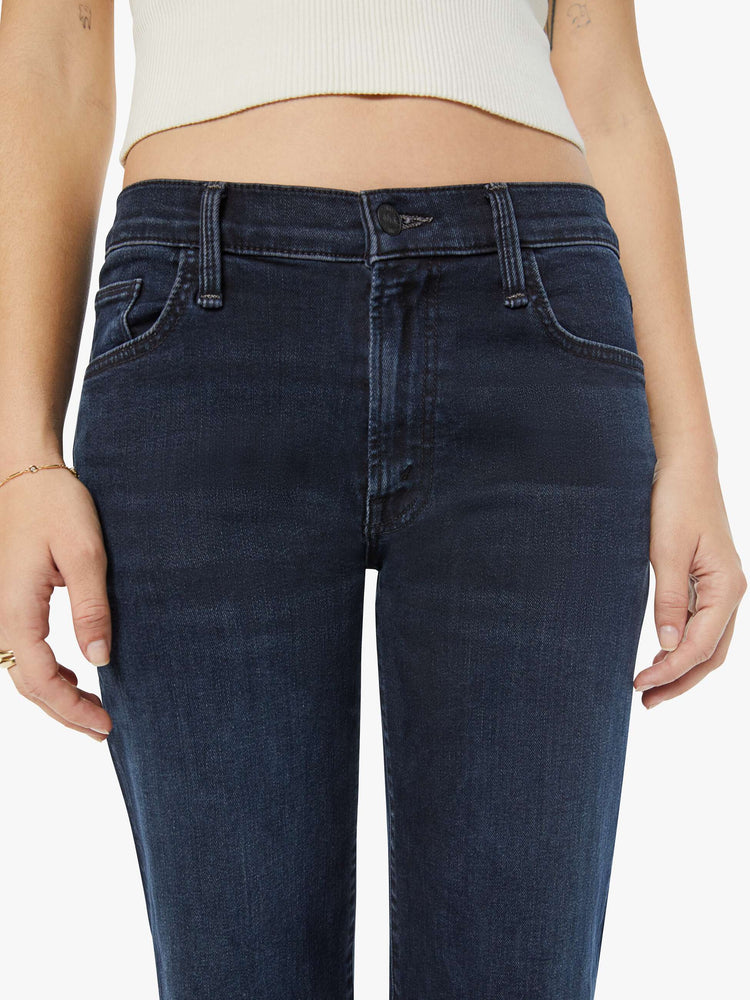 Waist close up view of a petite woman in a dark denim mid-rise jean with a wide straight leg, zip fly and clean ankle-length inseam.