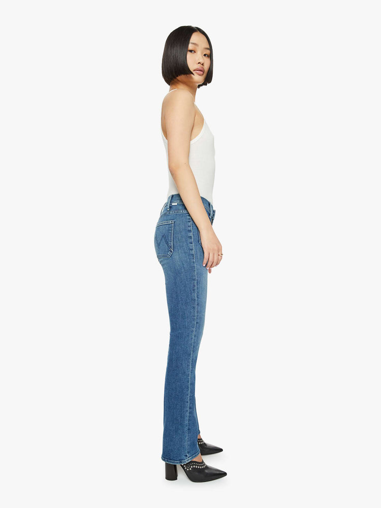 Side view of a woman in petite's medium blue high-rise bootcut designed with front patch pockets, a long inseam and a clean hem.