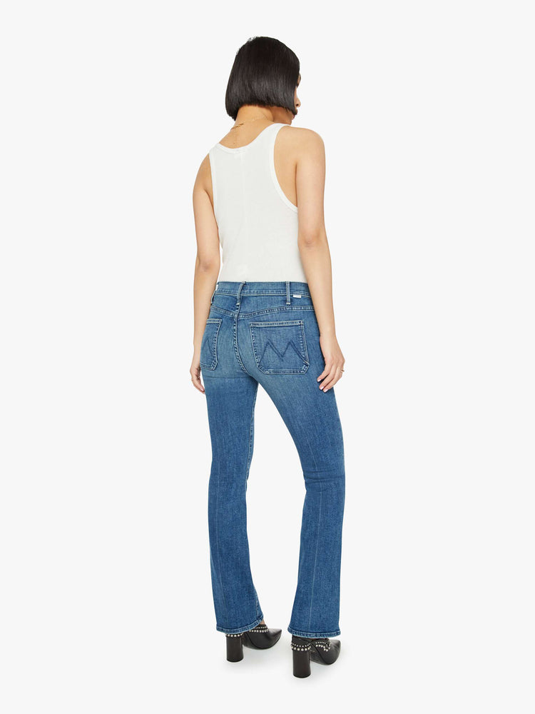 Back view of a woman in petite's medium blue high-rise bootcut designed with front patch pockets, a long inseam and a clean hem.