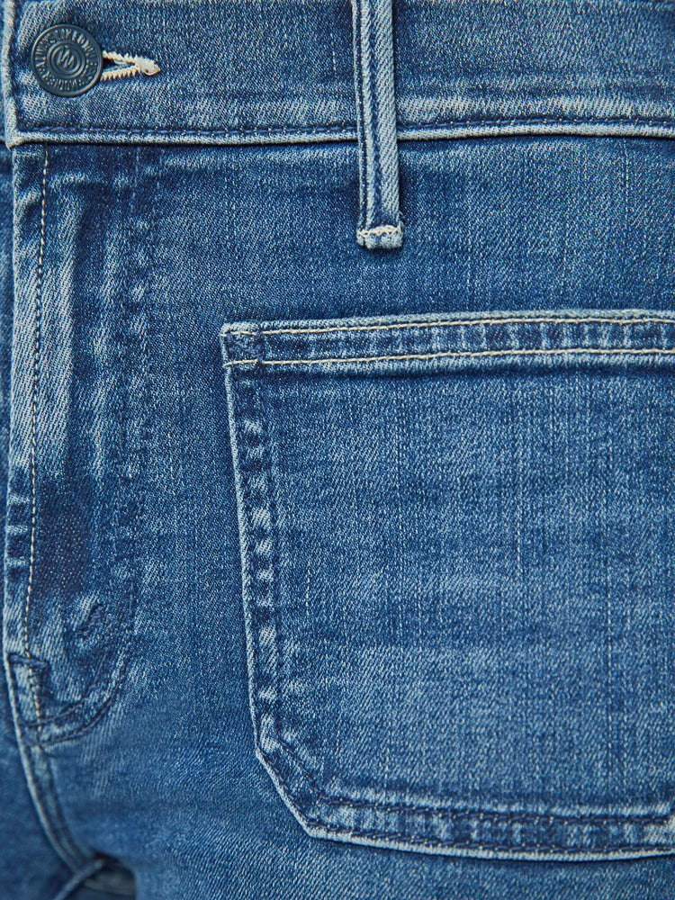 Detailed view of a woman in petite's medium blue high-rise bootcut designed with front patch pockets, a long inseam and a clean hem.