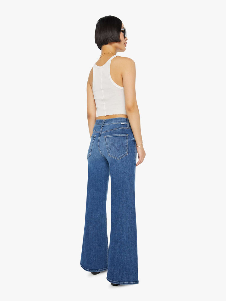 Back view of a petite woman in a mid-blue high-waisted wide leg has a button fly, 30-inch inseam and clean hem.