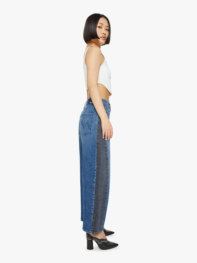 Side view of a petites woman in a black and blue super high-waisted jean with a wide, curved leg, a 26.25-inch inseam and a clean hem.