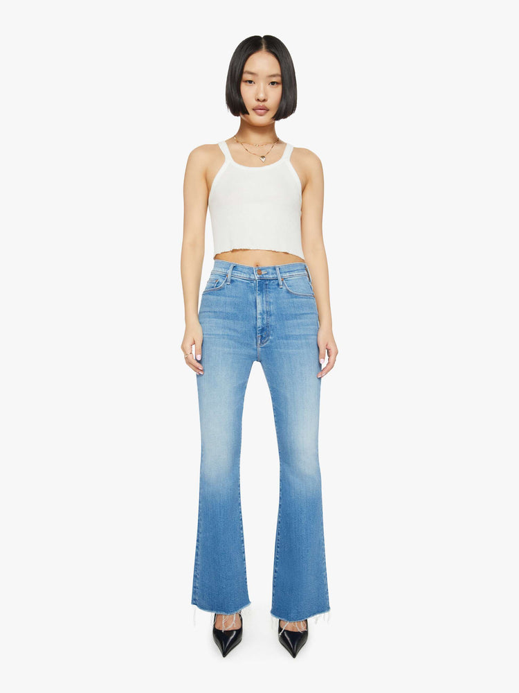 Front view of a petite woman in medium blue flare  jean has a high rise with a 29-inch length inseam and a frayed hem. 