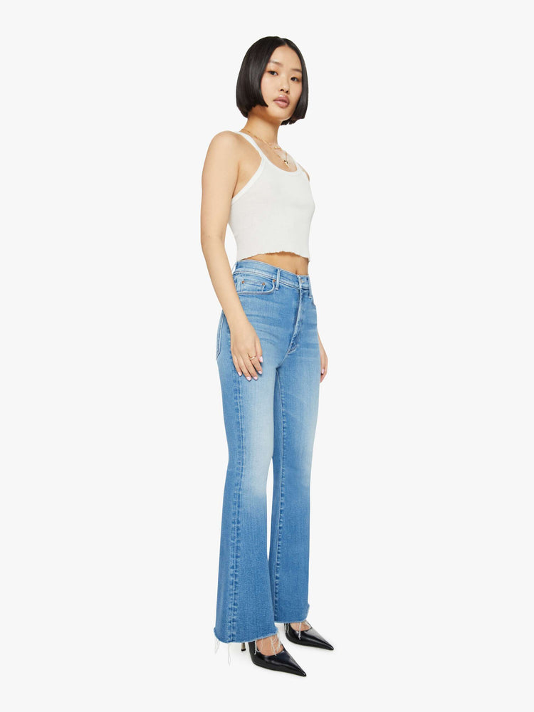 Side angle view of a petite woman in medium blue flare  jean has a high rise with a 29-inch length inseam and a frayed hem. 