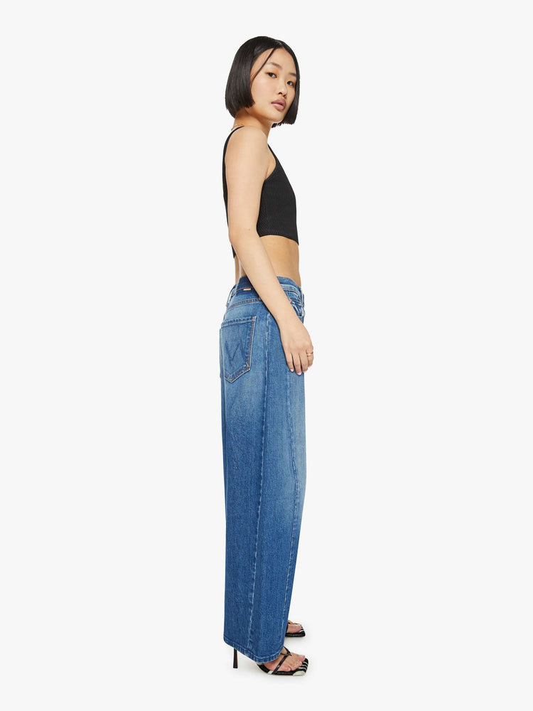 Side view of a petites woman in a super high-waisted pants with a full barrel leg, a 26.25-inch inseam and a clean hem in a med blue.