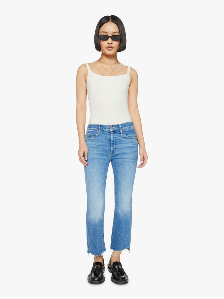 Front view of a petites woman high-waisted bootcut is cropped at the ankle with a frayed step-hem in a med blue wash.