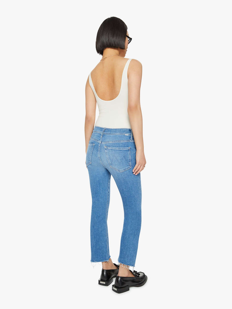 Back view of a petites woman high-waisted bootcut is cropped at the ankle with a frayed step-hem in a med blue wash.