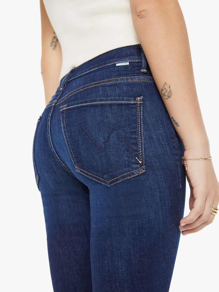 Back waist view of a petite woman in a dark blue wash high-waisted bootcut is cropped at the ankle with a frayed step-hem jean.