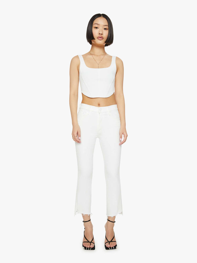 Front view of a petites woman high-waisted bootcut is cropped at the ankle with a frayed step-hem in a white wash.