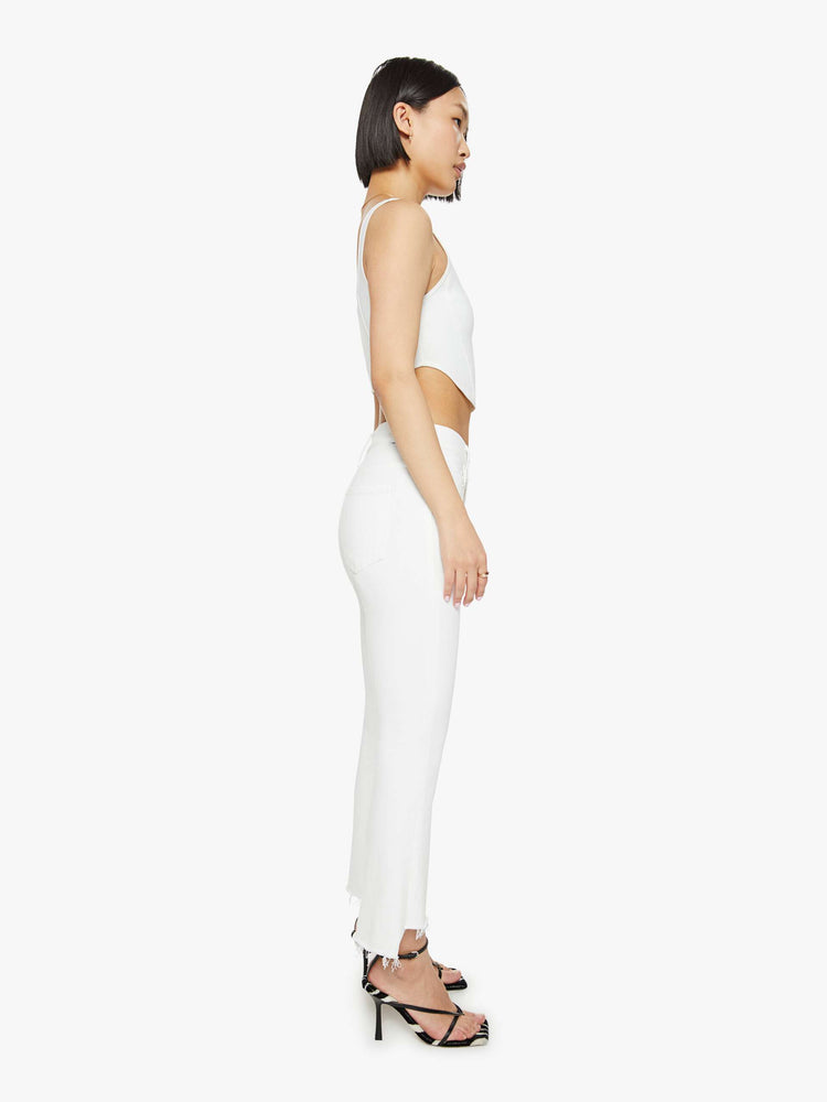 Side view of a petites woman high-waisted bootcut is cropped at the ankle with a frayed step-hem in a white wash.