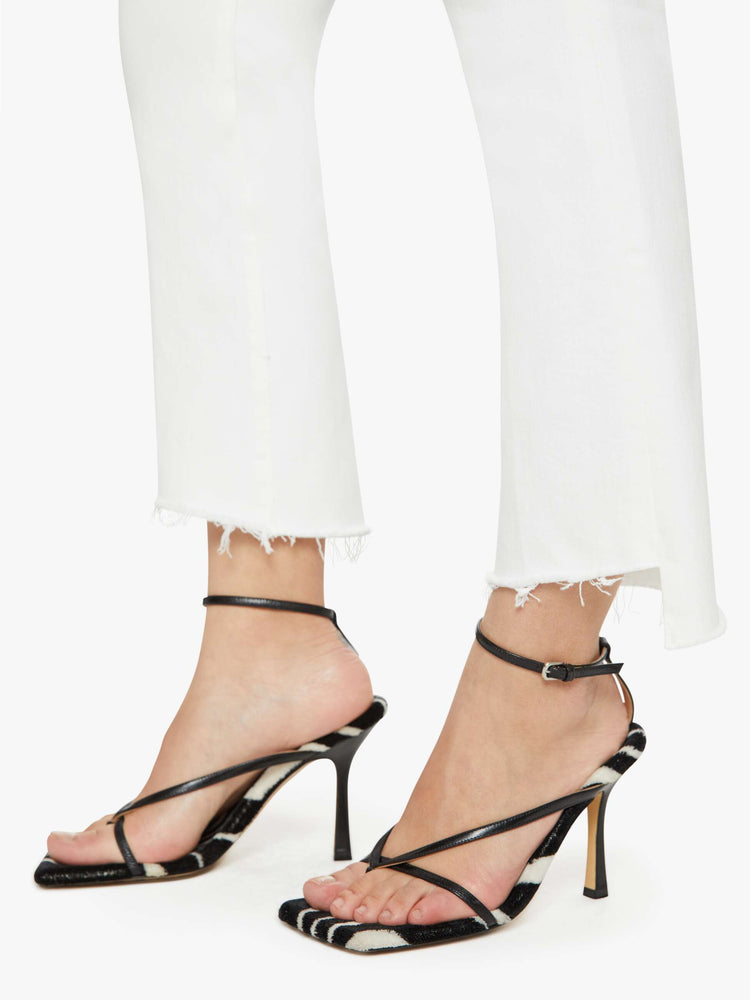 Hem view of a petites woman high-waisted bootcut is cropped at the ankle with a frayed step-hem in a white wash.