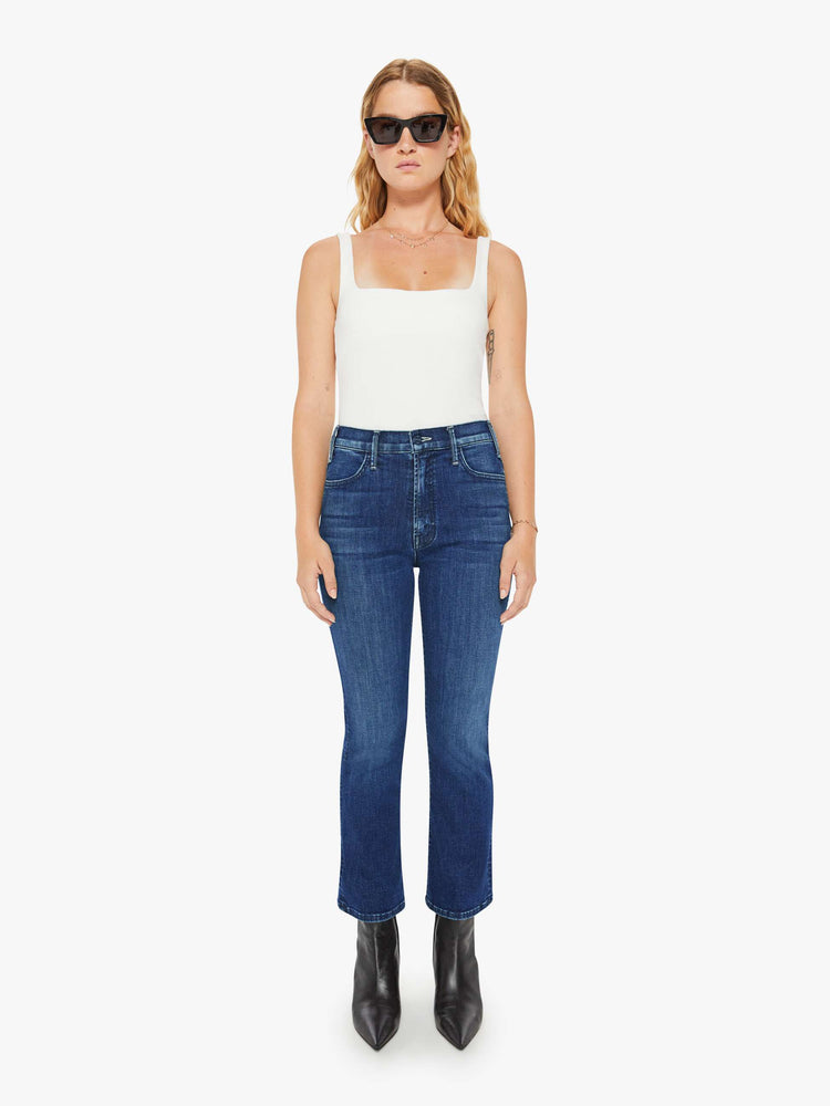 Front view of a petite woman in a dark blue wash high-rise flare has an ankle-length inseam and a clean hem. 