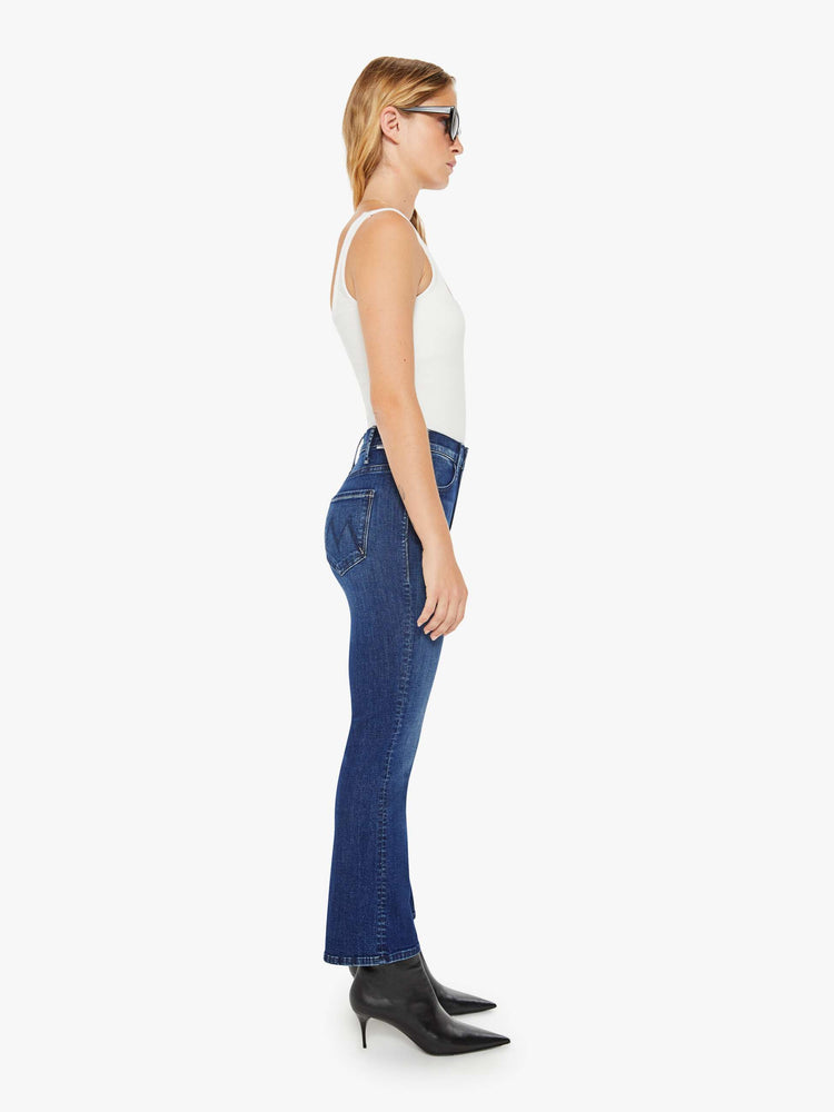 Side view of a petite woman in a dark blue wash high-rise flare has an ankle-length inseam and a clean hem. 