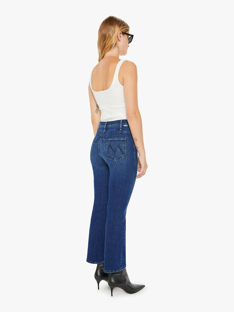 Back view of a petite woman in a dark blue wash high-rise flare has an ankle-length inseam and a clean hem. 