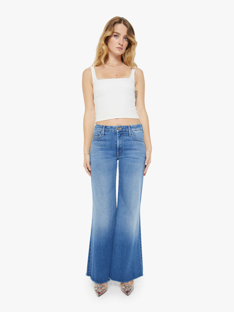 Front view of a petite woman in a high-waisted wide leg has a 31-inch inseam and a frayed hem mid blue jean.