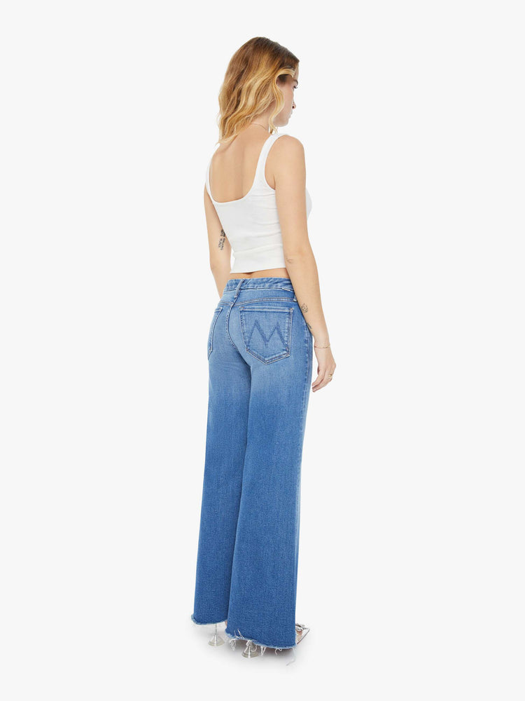 Back view of a petite woman in a high-waisted wide leg has a 31-inch inseam and a frayed hem mid blue jean.