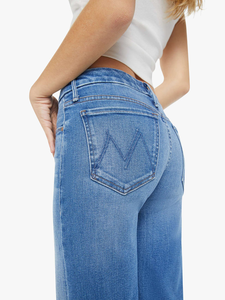 Waist view of a petite woman in a high-waisted wide leg has a 31-inch inseam and a frayed hem mid blue jean.